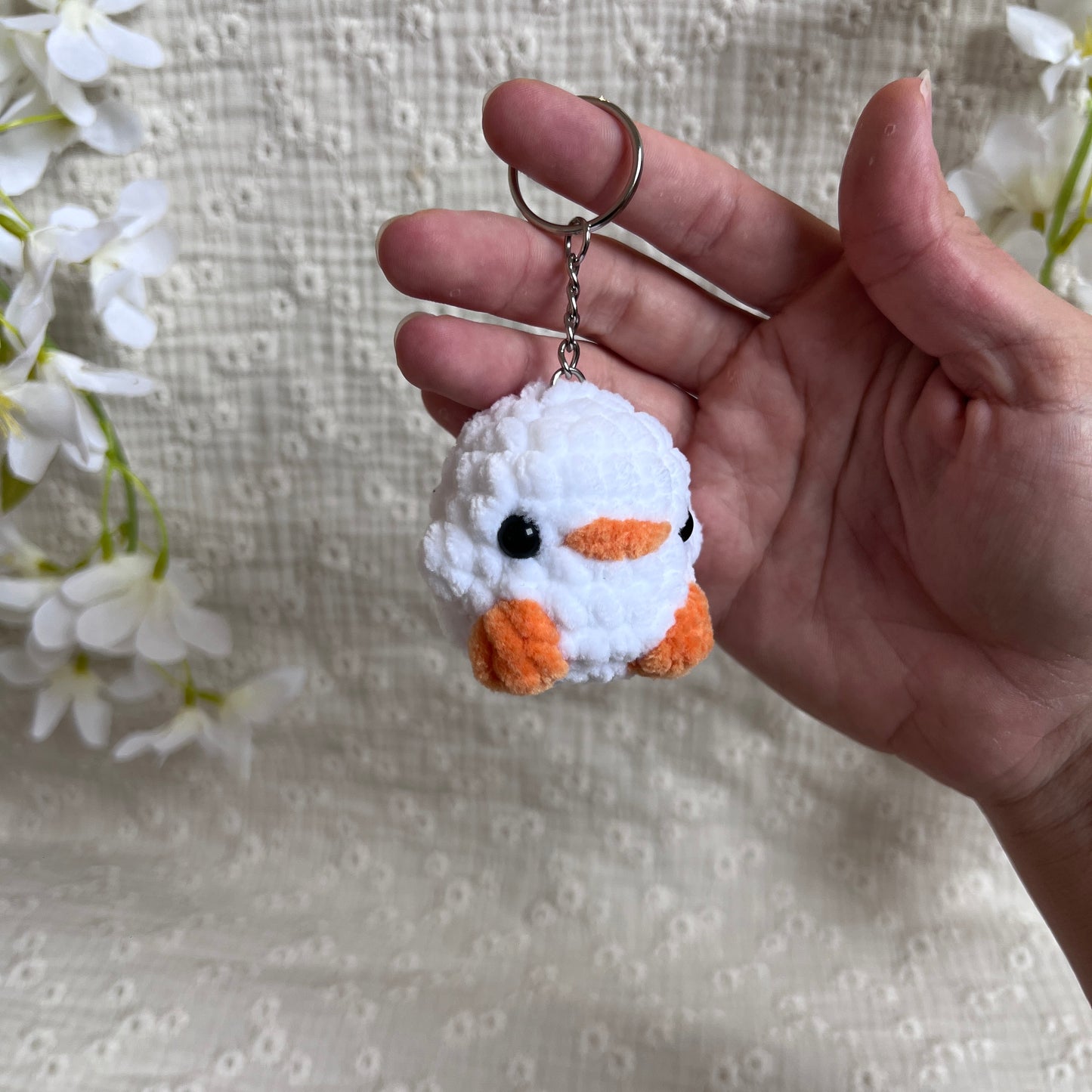 Porte-clés poussin blanc en crochet artisanal vu de trois quarts, mini amigurumi doux avec bec et pattes orange.